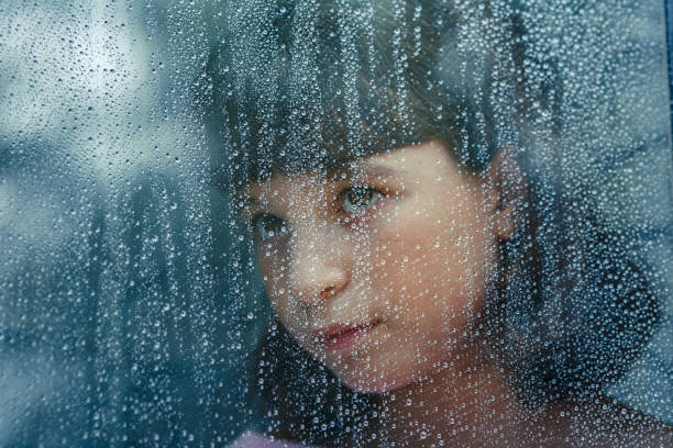 istock Sad child looking through wet window during rainy day 2185893789