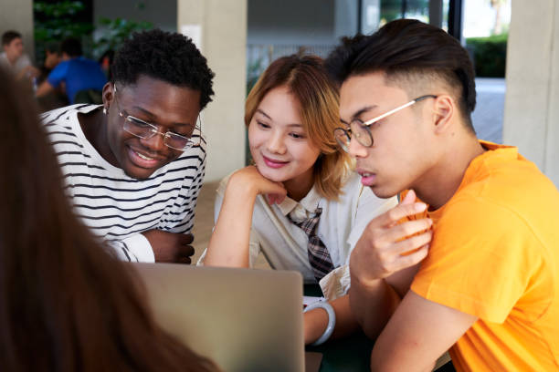 istock Group of Young People Sitting Around a Table using a laptop to work together in a group project. 2185898420