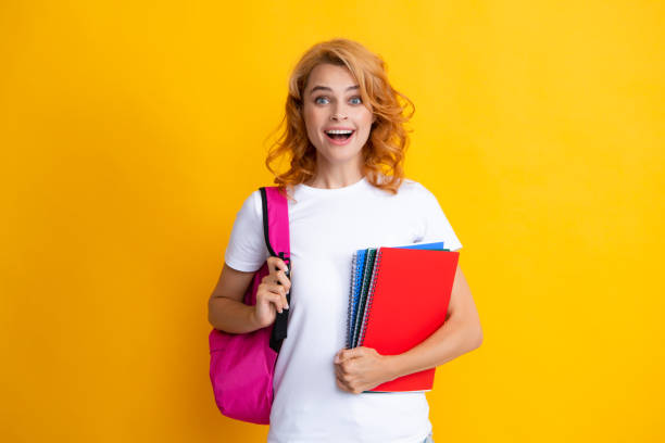 istock Cute student woman with backpack holds some documents and books over yellow background. 2185900869
