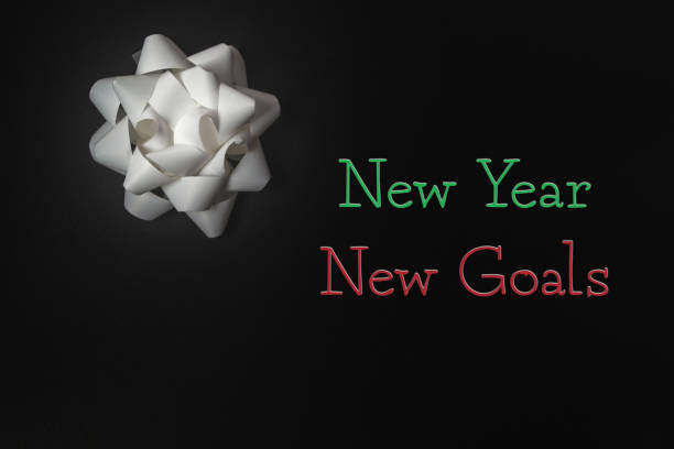 White bow with green and red accents on it. The bow is on a black background with the words New Year, New Goals written below it