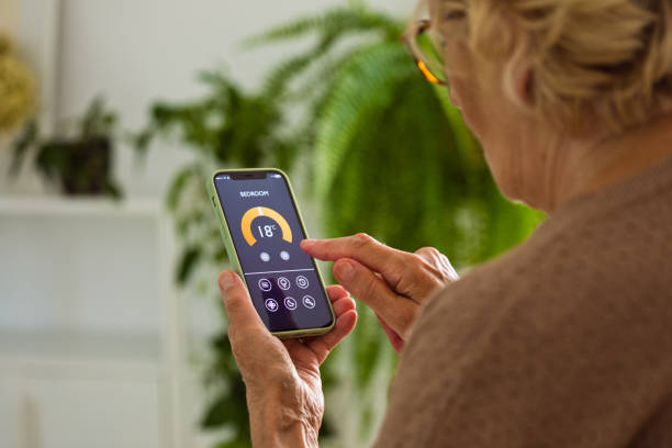 istock Senior woman using mobile phone to control termostat at home 2185907813