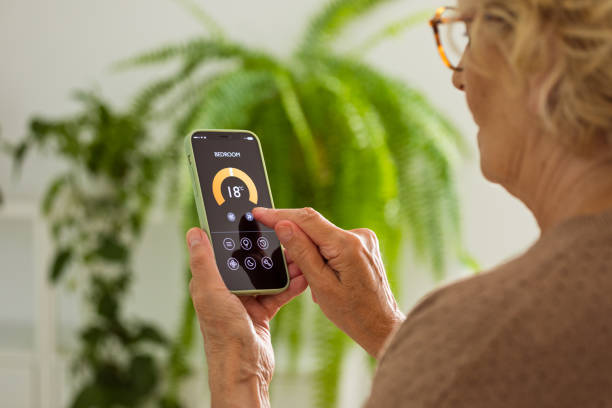 istock Senior woman using mobile phone to control termostat at home 2185907846