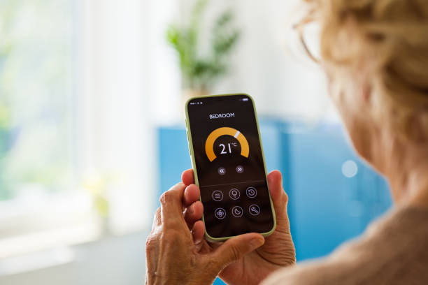 istock Senior woman using mobile phone to control termostat at home 2185907862
