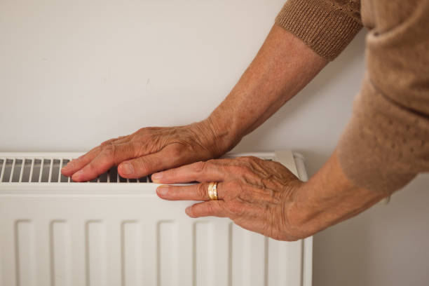istock Senior woman warms up hands over heater 2185907975