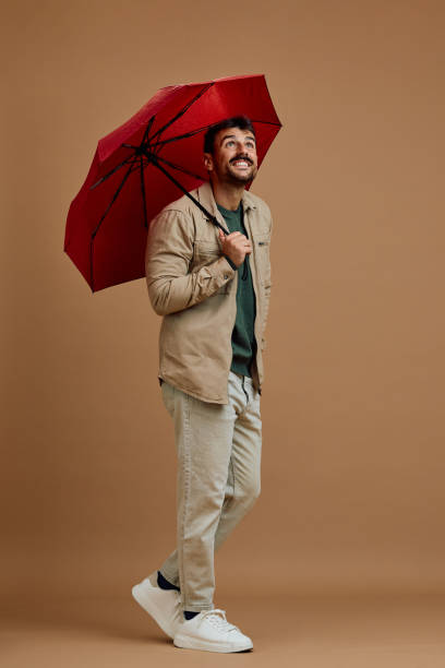 istock Studio shot of happy man with red umbrella looking up while walking. 2185909224