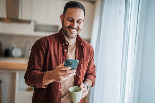istock A middle-aged handsome man is standing in the kitchen, drinking coffee and using a smartphone. 2185912305