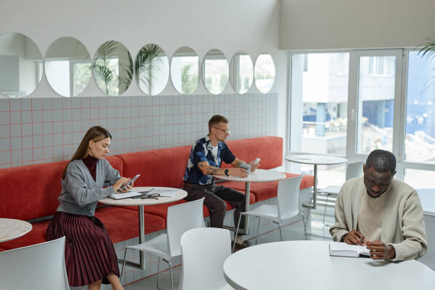 Wide angle shot of African American businessman writing in notebook while sitting at table in cafe of coworking space. Business people working in cozy cafe featuring modern minimalistic design