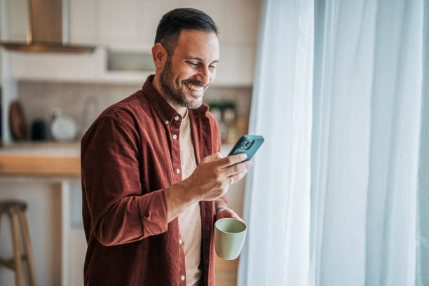 istock A middle-aged handsome man is standing in the kitchen, drinking coffee and using a smartphone. 2185912746