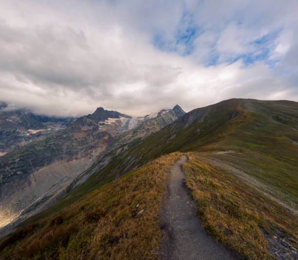 A breathtaking view of an expansive alpine valley framed by rugged peaks and dramatic clouds, showcasing nature's grandeur and tranquility.