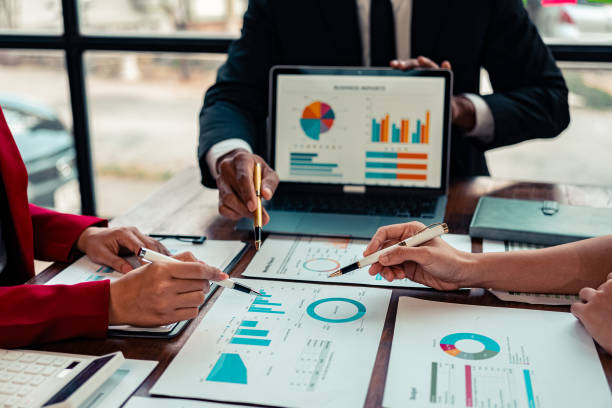 istock A business meeting or discussion involving financial reports, charts, and data analysis. Participants are reviewing a visual presentation, likely discussing performance metrics or strategies. 2185928799