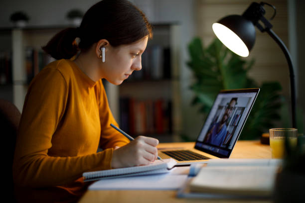 istock Teenage girl with wireless headphones taking notes while watching an online tutorial on her laptop at home 2185949175