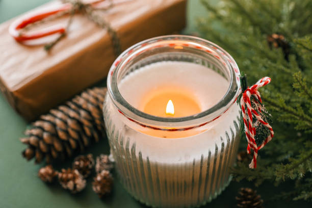 istock A lit candle in a festive glass holder surrounded by pinecones, evergreen branches, a wrapped gift, and a candy cane, creating a cozy Christmas mood with warm and inviting light 2185949933