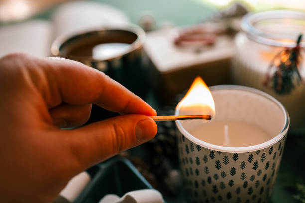 istock A hand lighting a festive candle with a matchstick, surrounded by pinecones, marshmallows, and evergreen branches, creating a warm and cozy Christmas atmosphere 2185949947