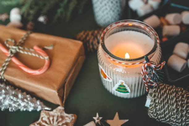 istock Cozy Christmas setup featuring a wrapped gift with a candy cane, a lit candle, tea, an open book, pinecones, marshmallows, and evergreen branches on a green background 2185949961