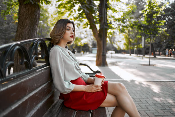 istock cute blonde sitting on a park bench resting a cup of coffee 2185950575
