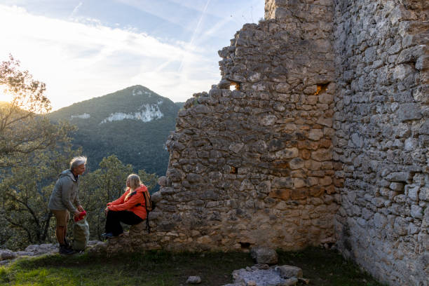 Mature couple sit on wall in old ruin above hills at sunset, Liguria
