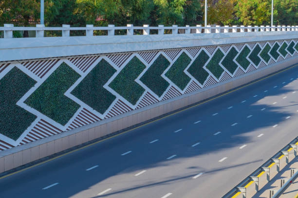 The side direction signs on eight-lane highway are saddled with green artificial plants. On the asphalt there is discontinuous white and yellow solid strip, dividing metal bumpers, no cars, no people. las señales laterales de dirección en la autopista de ocho carriles están llenas de plantas artificiales verdes. sobre el asfalto hay una franja sólida discontinua blanca y amarilla, parachoques metálicos divisorios, no hay coches, no hay personas
