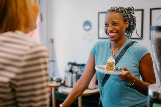 A customer smiles at her barista while holding a slice of cake
