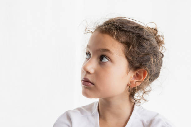 Thoughtful girl looking up, side profile on white background, copy space.