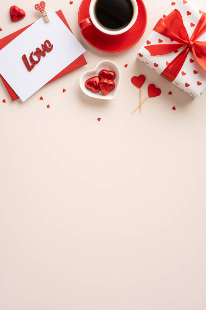 istock Romantic Valentine's Day vertical setup featuring a gift with red hearts, a love card, and a cup of coffee on a table 2185957250
