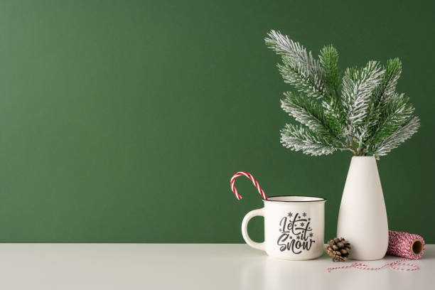 istock A side view minimalist Scandinavian winter scene featuring a white mug with holiday text, a vase with pine branches, and a candy cane, set against a green background 2185957302