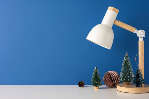 istock Minimalist side view Scandinavian desk scene featuring a modern lamp and decorative mini Christmas trees against a blue wall, capturing cozy winter vibes 2185957314