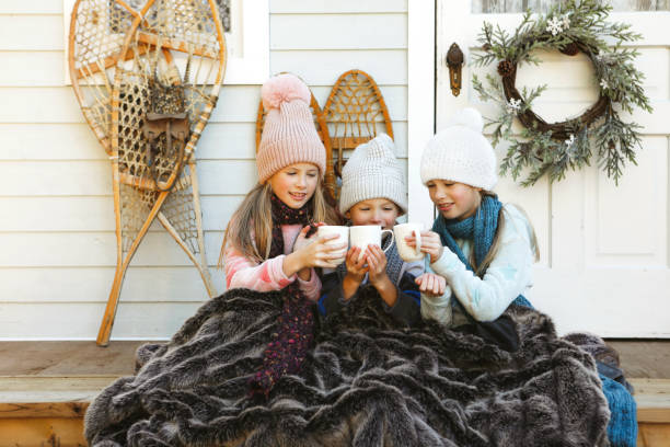 Three siblings sit on a charming, rustic porch, drinking hot chocolate.