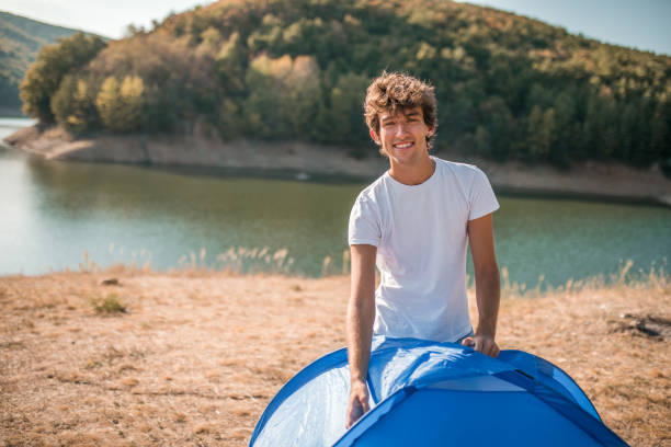 istock Portrait of a smiling young man looking directly into the camera while setting up a camping tent on the shore of a lake 2185970180