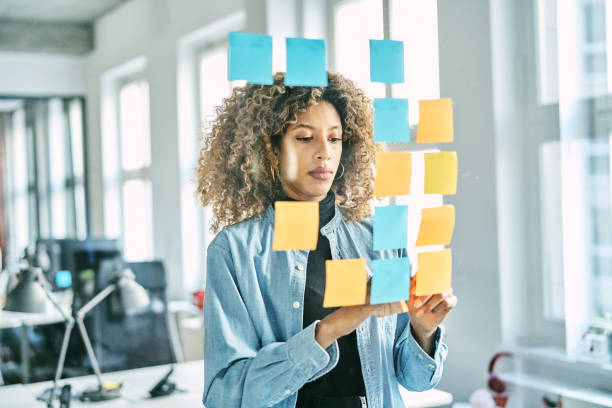 Young woman putting sticky notes on a glass wall while working on a new project in office