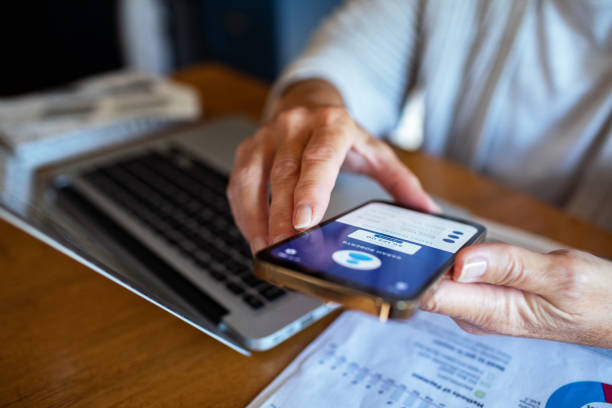 istock Mature woman using a banking app on her smart phone while going over her bills and home finances 2185973017