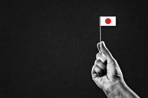 Hand in Black and White Holding Japanese Flag, Black Textured Background with Copy Space