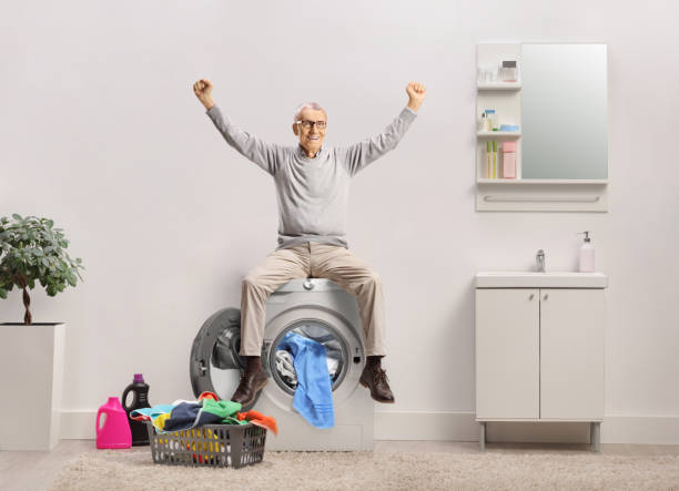 istock Happy elderly man raising arms and sitting on a washing machine 2185977497