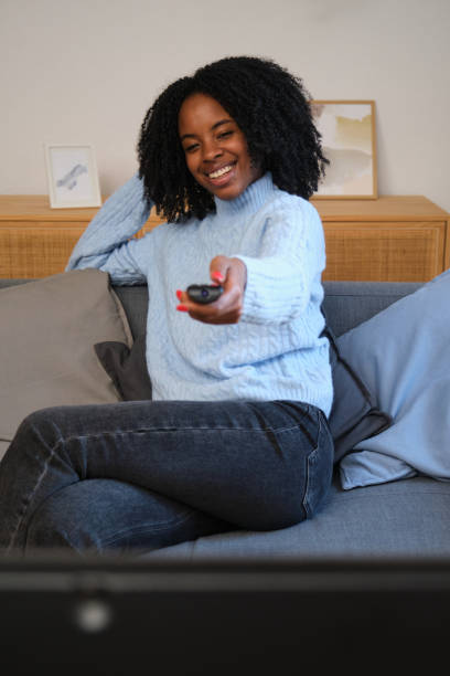 istock Young woman sitting on sofa watching tv and holding remote control 2185982998