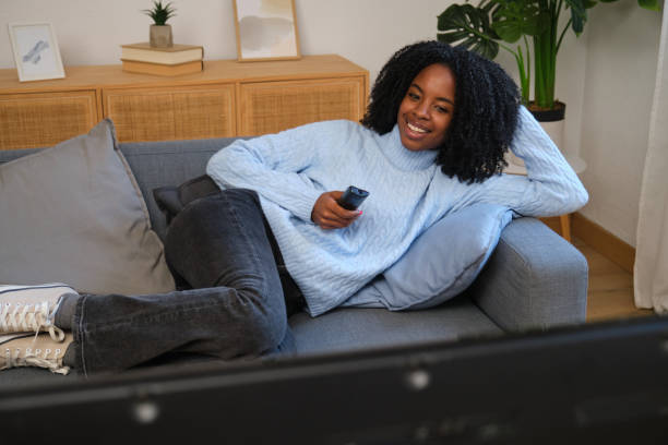 istock Young woman relaxing on sofa watching television and holding remote control 2185983024