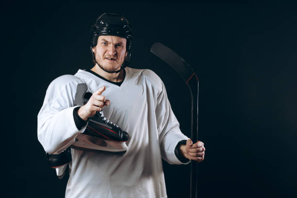 istock Confident hockey player looking at camera with skate in hand. Isolated on black. 2185985829