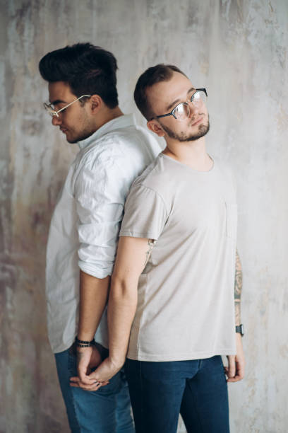 Full length portrait of two upset young men standing back to back with arms folded isolated over white background