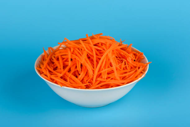 Thinly sliced ​​carrots in a white bowl over blue background. Home cooking.