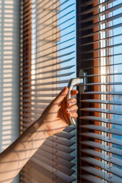 istock Hand adjusting window blinds to let sunlight in during a bright morning 2185993739