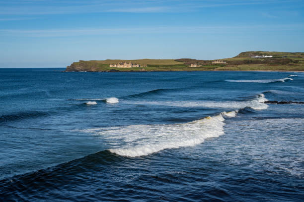 Portballintrae bay on a sunny warm day with Runkerry House in the distance on the coastline, on a windy day with waves crashing onto the sandy beach