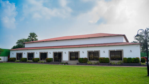 A well-organized conference room setup, with rows of tables covered in royal blue tablecloths and chairs dressed in white slipcovers. The room has a contemporary, minimalist aesthetic, with a high ceiling featuring circular light fixtures and stylish paneling on the walls. Large windows on one side allow natural light to brighten the space, complementing the modern interior design. This layout is ideal for corporate events, seminars, and training sessions, providing a professional and clean environment.