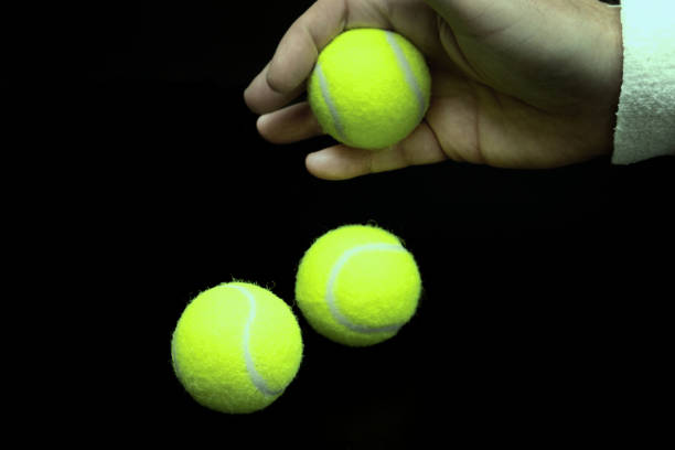 istock Hand dropping tennis balls on black background with copy space 2186003297