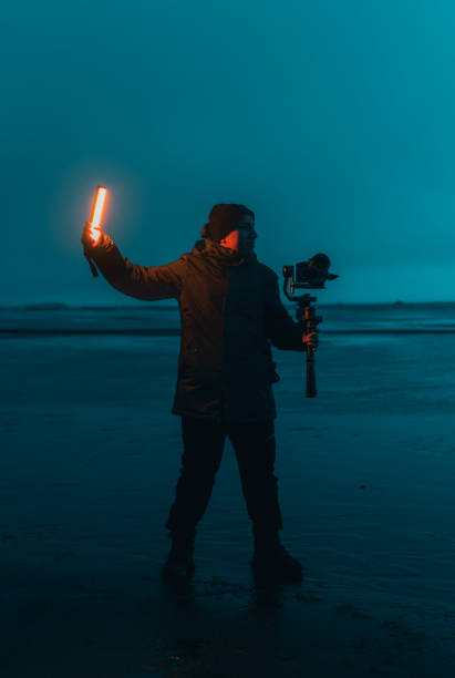 istock Videographer holding led light wand and gimbal at beach during blue hour 2186018031