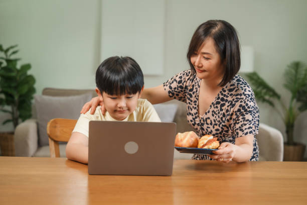 istock An Asian mother and son sit at the table and sofa, sharing time together while looking at a computer, tablet, and phone. They bond through technology and family activities 2186025663