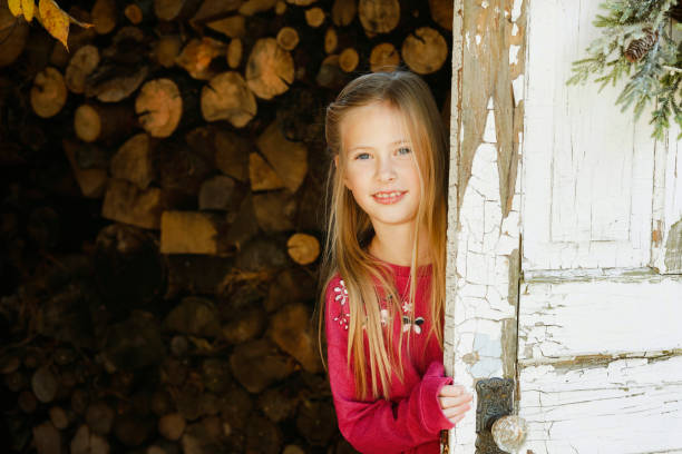 A beautiful, eight-year-old girl smiles at the camera as she peeks out from behind a door. Shot with a Canon 5D Mark IV.