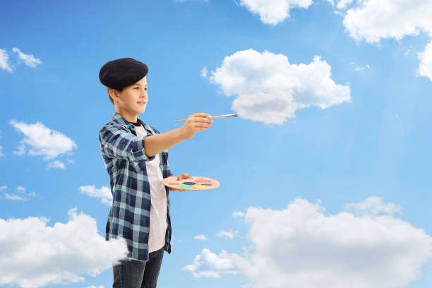 Boy painting clouds with a paintbrush in the sky