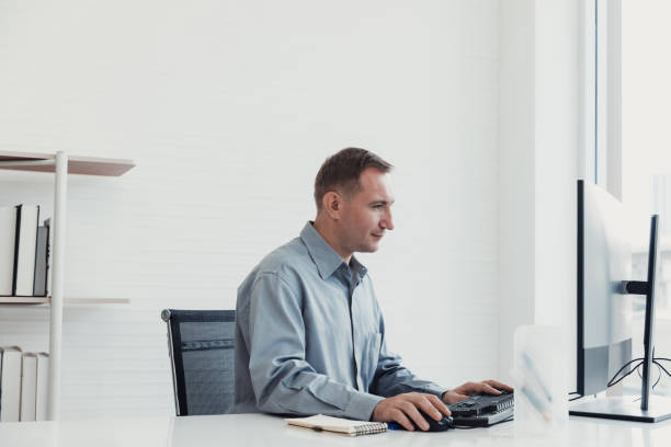 We look over a Customer service operator's shoulder as he works on his  computer. Focus on man