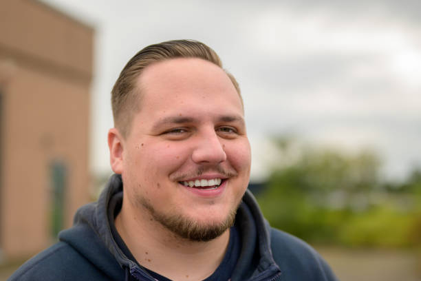 A cheerful close-up portrait of a smiling man in a dark hoodie. His neatly styled hair and light stubble highlight his warm and friendly expression.