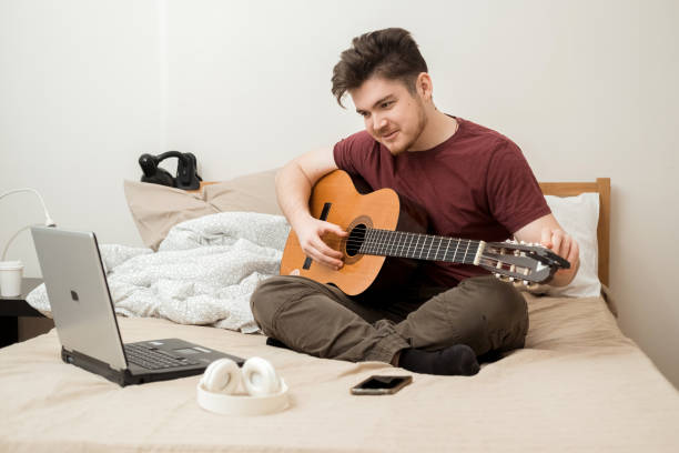 istock A young man is sitting on the bed and tuning his guitar. 2186071429