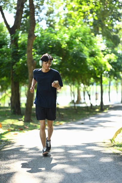 istock Active young man listening to music jogging on a sunny park pathway 2186075988