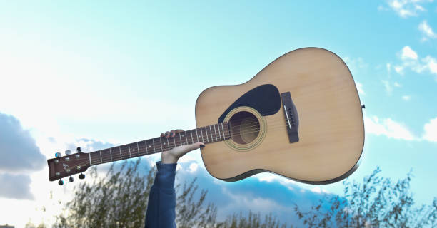 Close-up guitar in hand against blue sky background